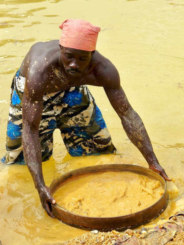 A man pans for diamonds in a muddy river in Sierra Leone, showcasing traditional mining methods.
